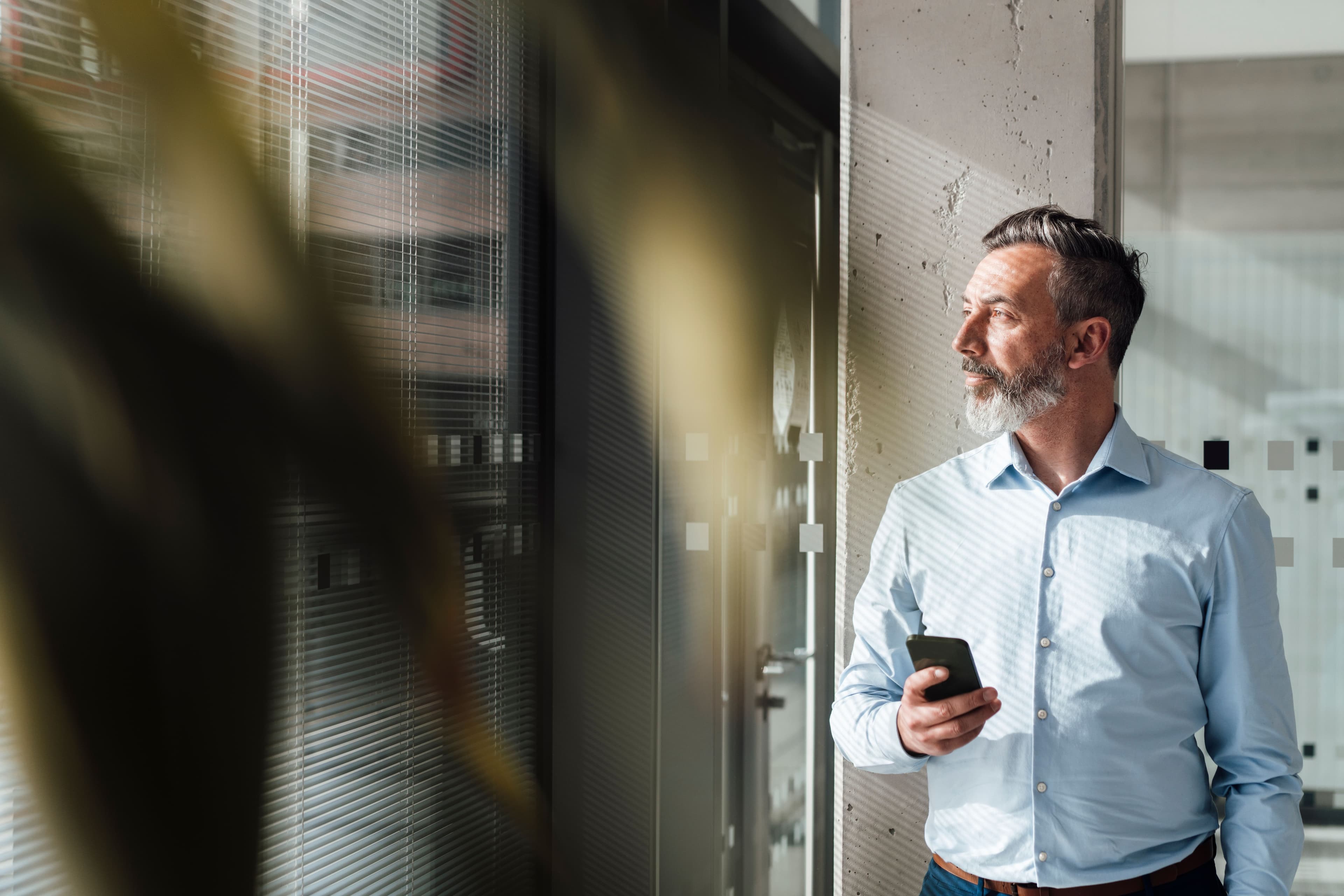 A professional holding a phone beside an office window.
