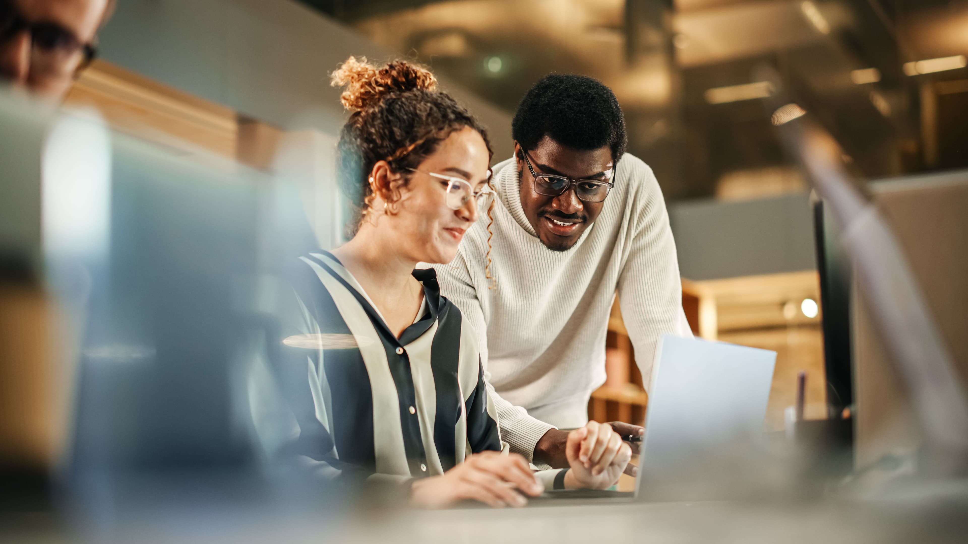 Two colleagues from different teams review data together on a laptop